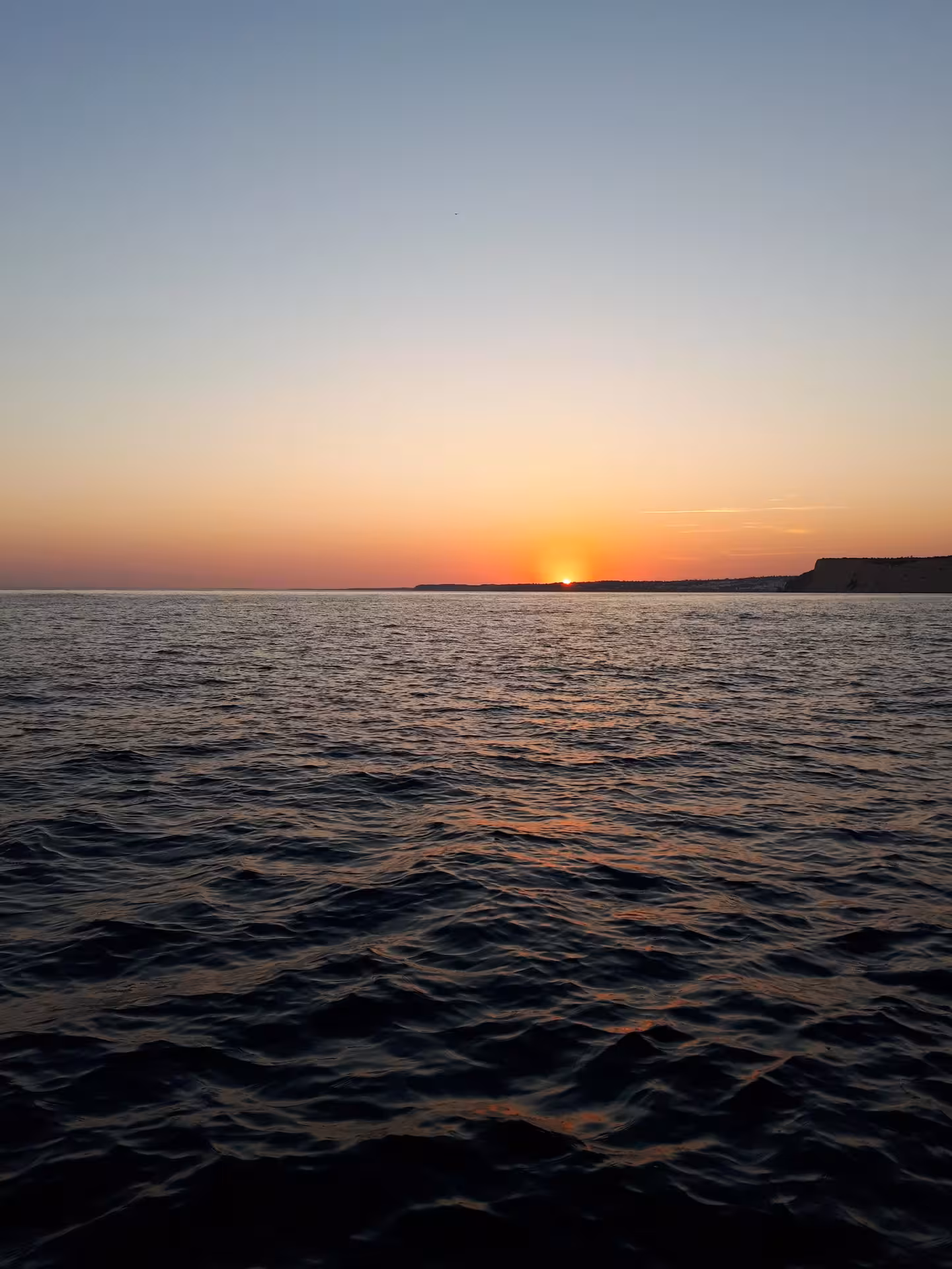 Golden sunset over the Atlantic on a Lagos Algarve catamaran cruise, calm sea and coastline on the horizon