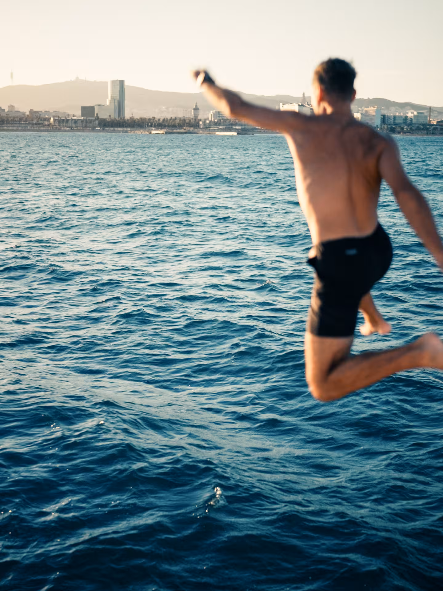 Guest jumping into the sea from a catamaran near the coast, fun sunset sailing tour with swim stop