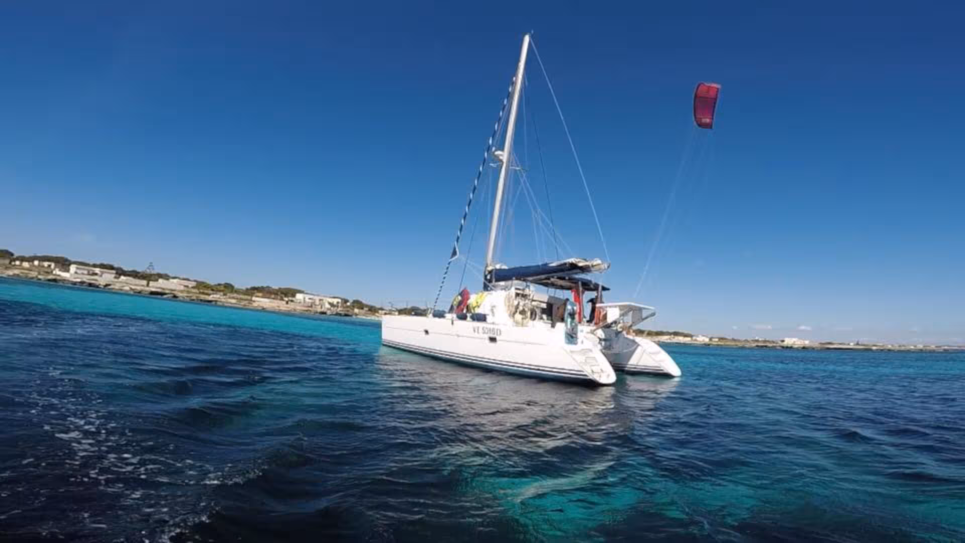 Catamaran Tenerè anchored in the vibrant blue waters of La Maddalena, ready for a scenic day tour from Cannigione.