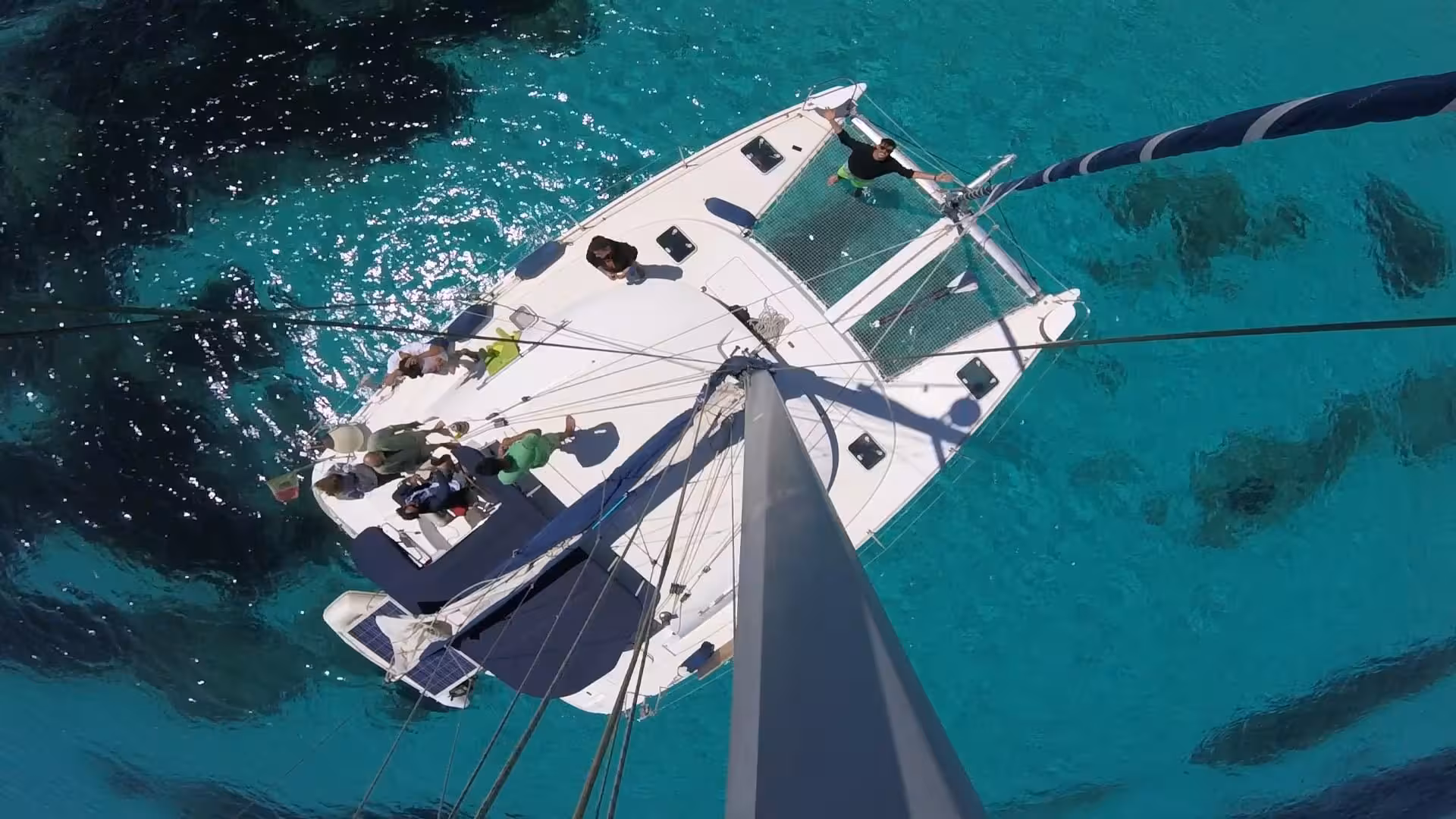 Aerial view of a catamaran sailing through the turquoise waters of La Maddalena Archipelago on a sunny day.
