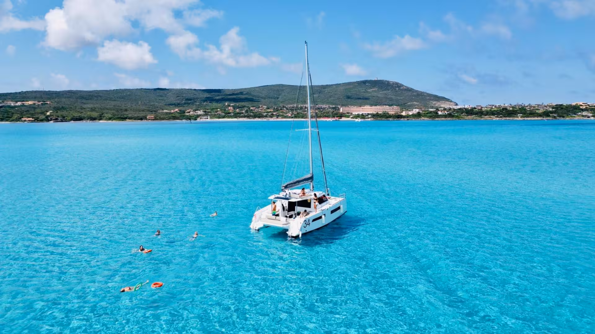 Catamaran anchored in the serene turquoise waters near La Pelosa, Stintino, with swimmers enjoying the sea.