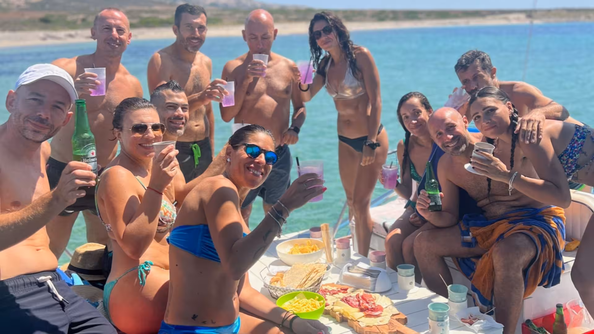 Group enjoying a festive gathering with drinks and snacks on a catamaran in the picturesque Gulf of Asinara.