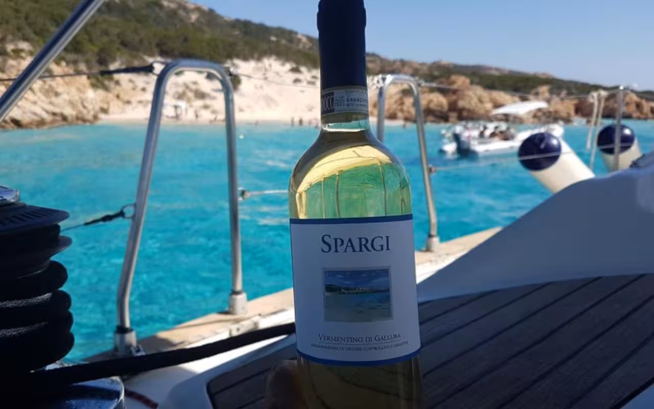 Bottle of Spargi wine on a catamaran with scenic views of La Maddalena's azure waters and rocky coastline.