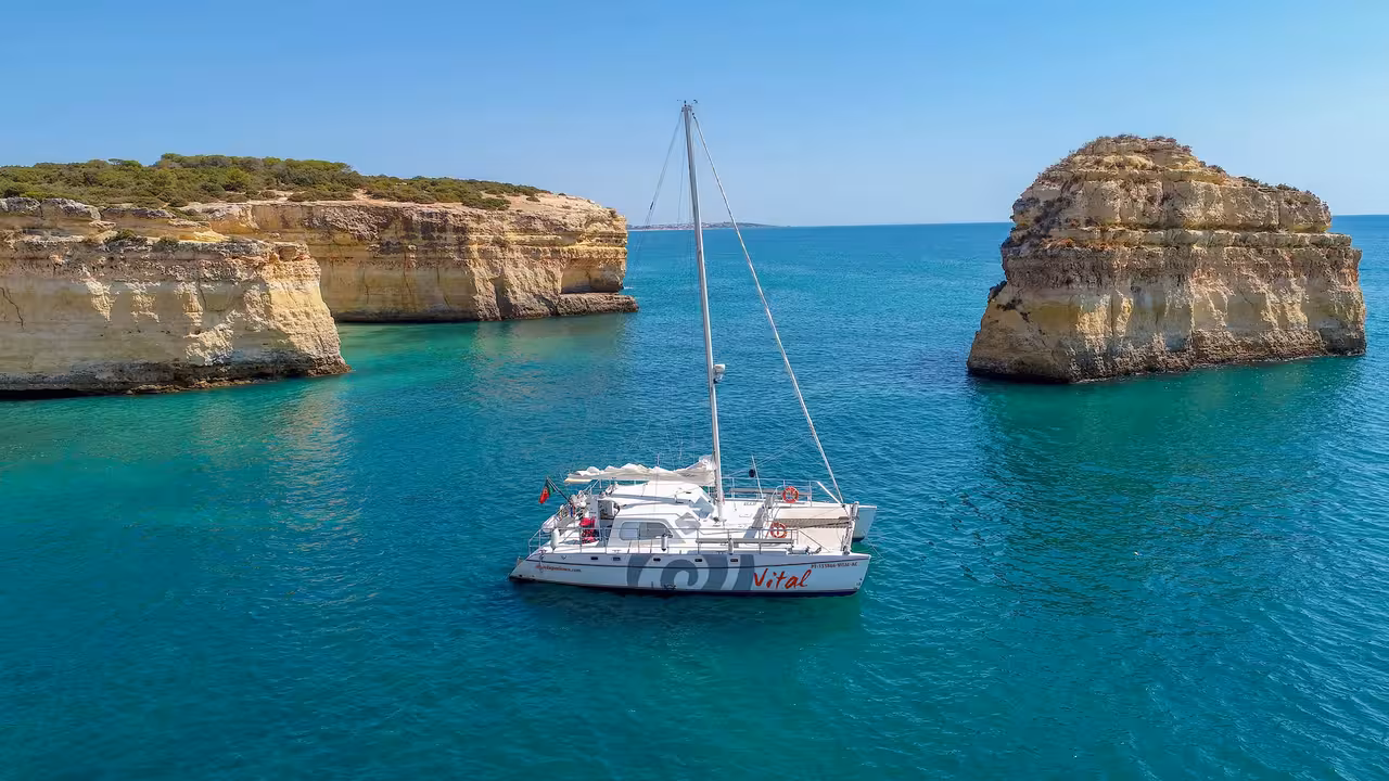 Aerial view of private catamaran anchored between stunning rock formations on turquoise waters near Lagos Algarve