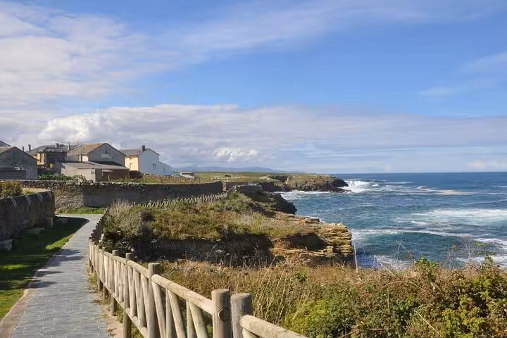Scenic coastal view of Pancha Island with ocean waves and rustic houses under a clear blue sky, ideal for Catedrais Beach tour.