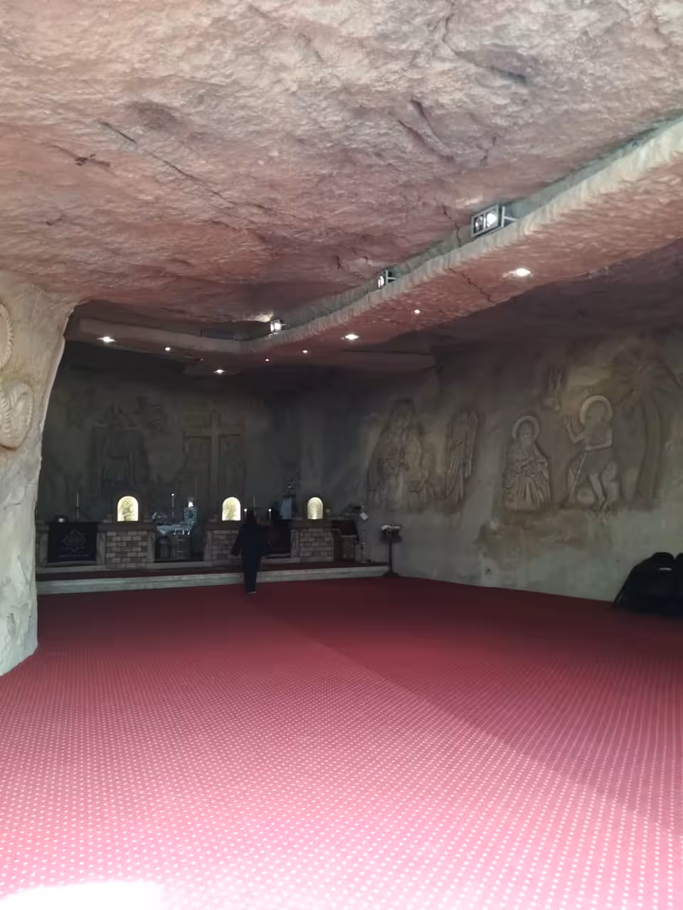 Cave church interior with carved stone reliefs and red carpet at Red Sea monastery