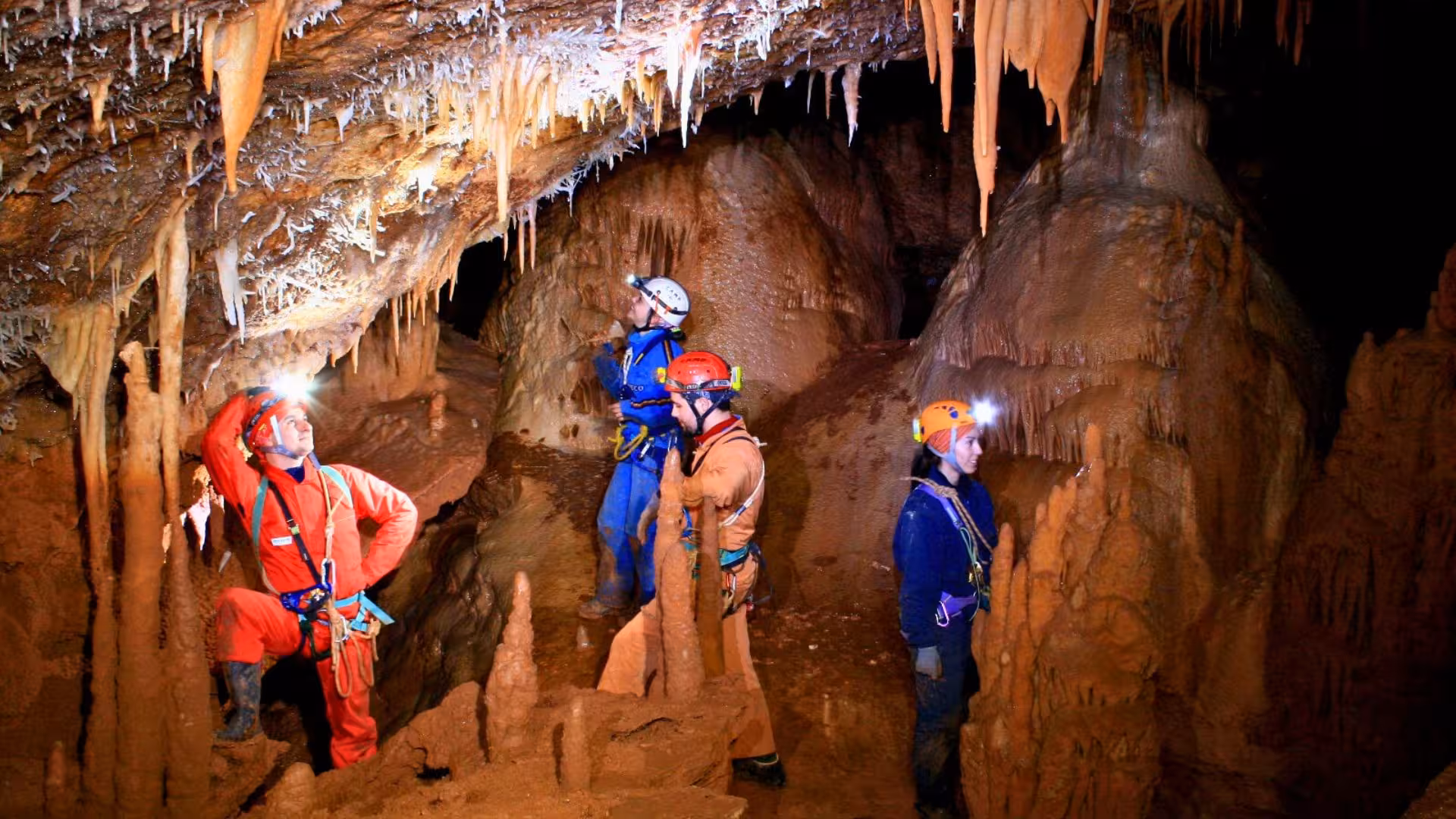 Group of cavers exploring the intricate cave systems of Dorgali, Sardinia, with stunning stalactites overhead.