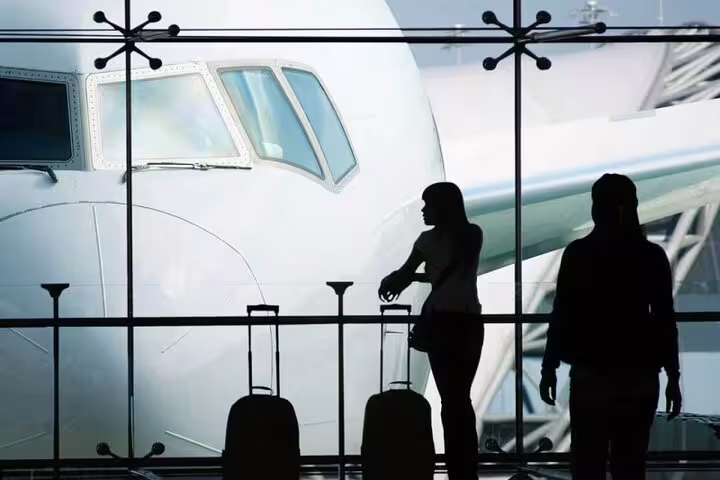 Travelers with luggage at CDG terminal window by airplane, waiting for private airport transfer to Paris
