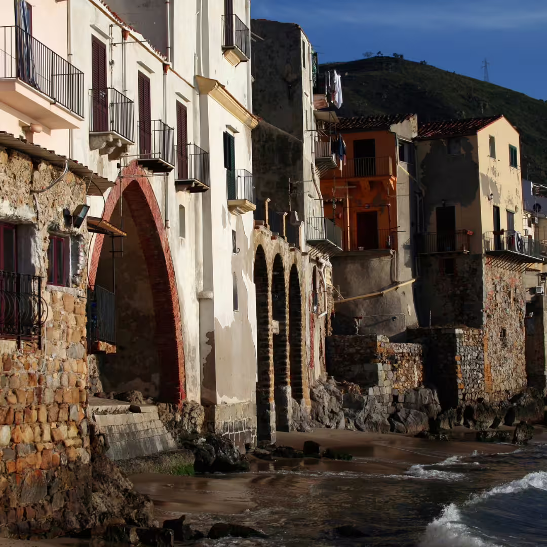 Historic seafront houses and arches of old Cefalù, Sicily, overlooking waves on a Palermo private day trip