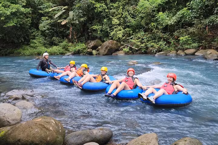 Group of smiling people tubing on the Celeste River, surrounded by lush greenery and vibrant blue waters.