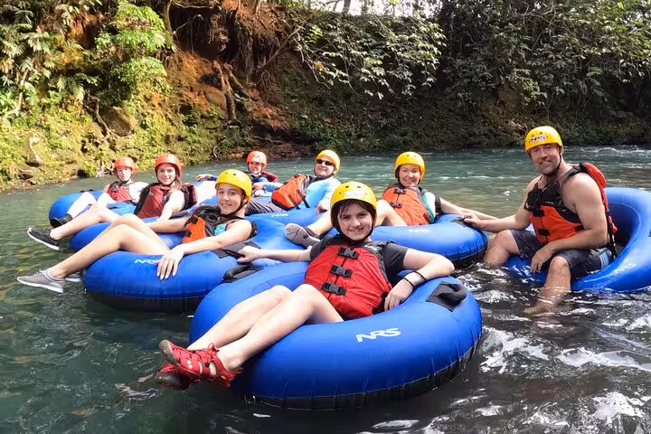 Smiling group of tubers relaxing on the Celeste River in bright safety gear under the canopy.
