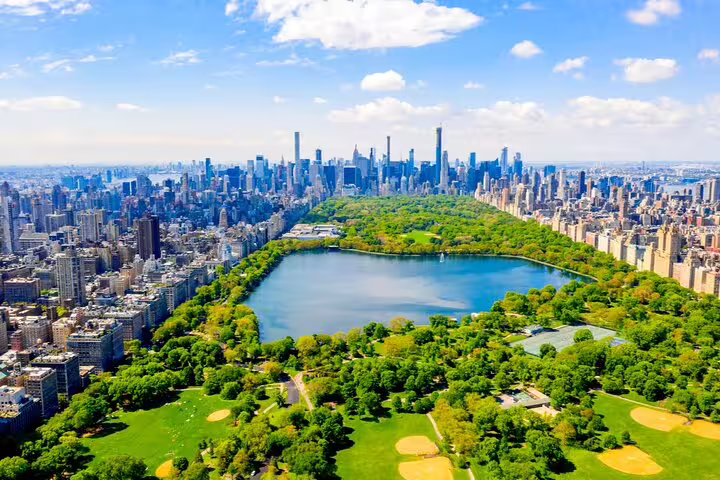 Aerial view of Central Park with lake, lush greenery, and Manhattan skyline on a sunny day