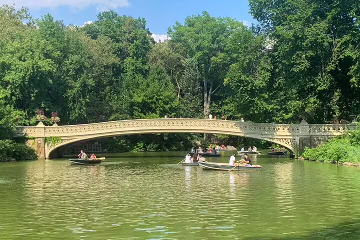 Bow Bridge in Central Park with rowboats on the lake surrounded by lush green trees