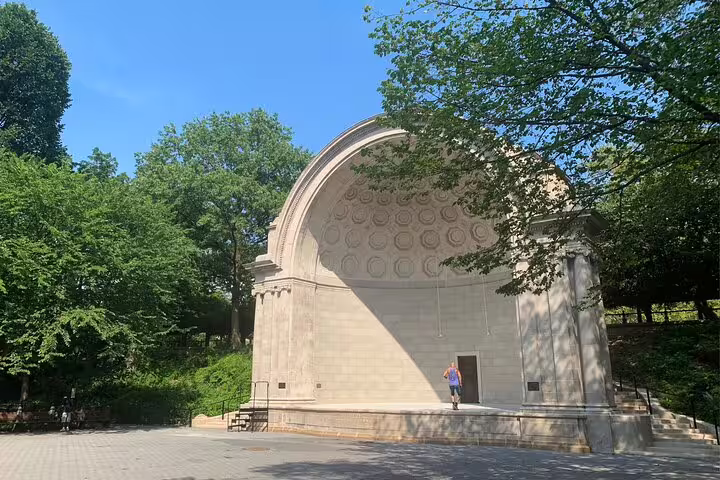 Naumburg Bandshell amphitheater in Central Park surrounded by lush green trees on a sunny day