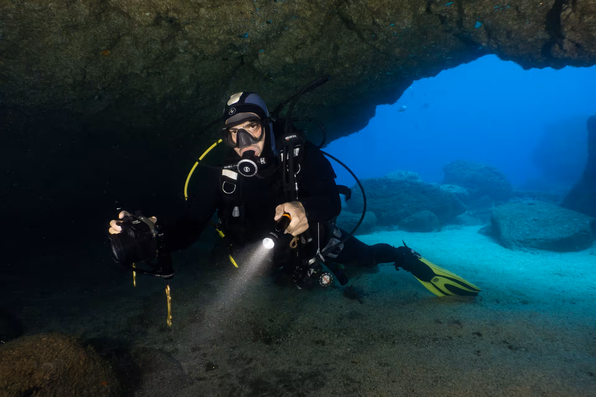 Certified diver explores underwater cave with flashlight during boat dive to national park or wreck.