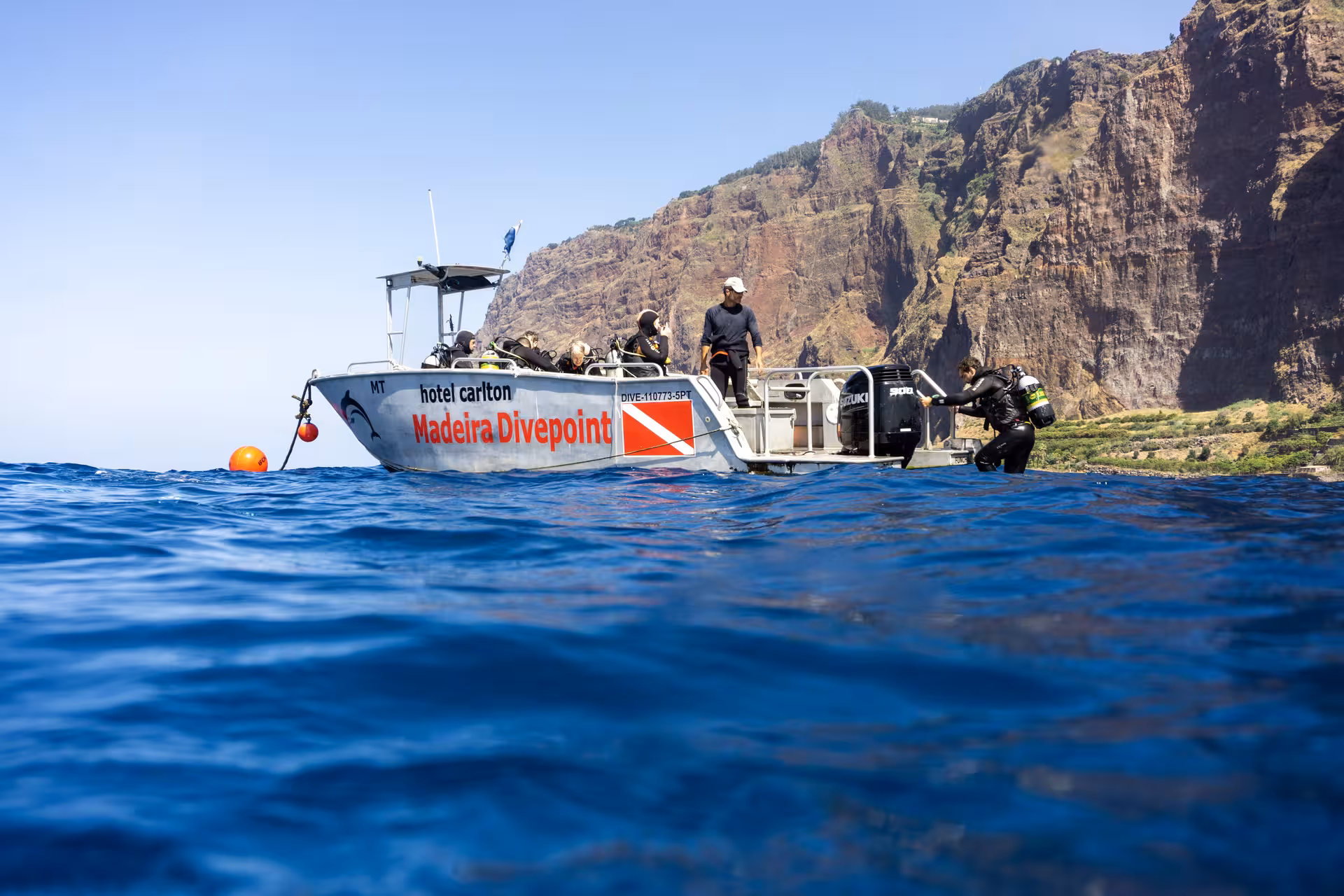 Divers prepare on a boat near scenic cliffs for an exciting certified dive trip to explore national parks or wrecks.
