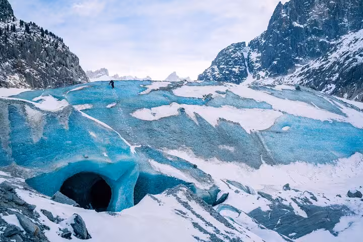 Blue glacial ice cave entrance at Chamonix with a hiker walking on the glacier above