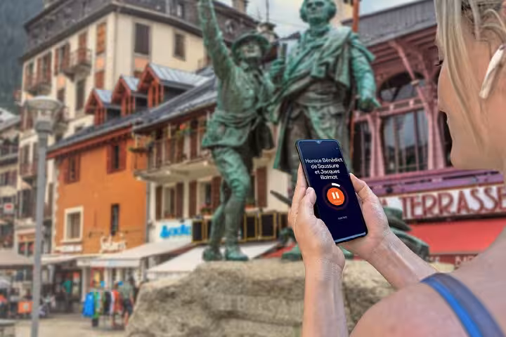 Tourist using audio guide app on smartphone in front of Saussure and Balmat statue in Chamonix