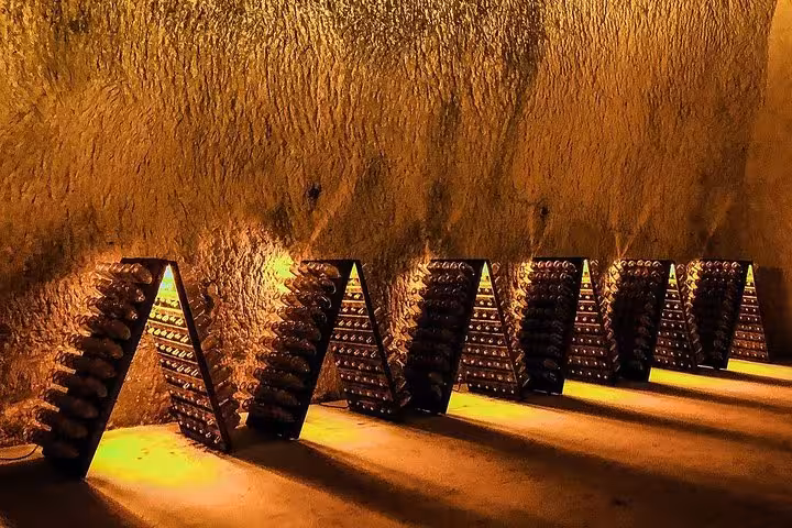 Wine bottles aging on riddling racks in a dimly lit Champagne cellar in Epernay, France