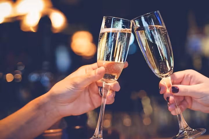 Two hands clinking champagne flutes in a toast at a glittering evening venue