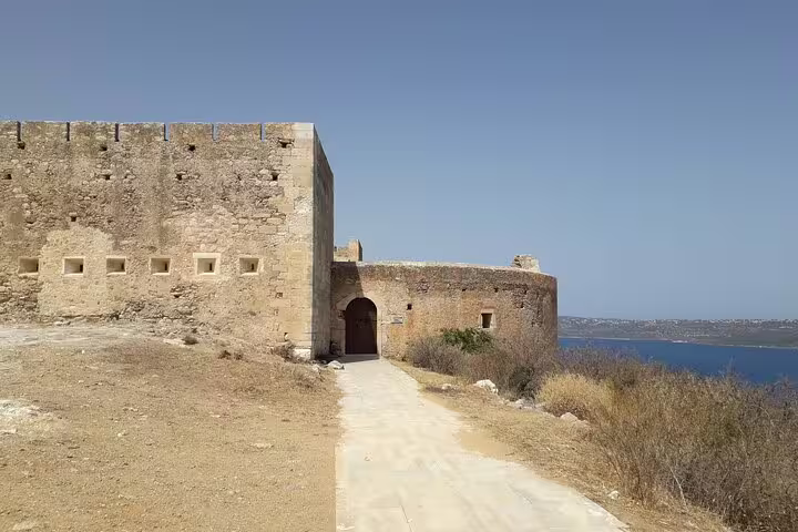 Ancient stone fortress in Chania with rustic walls and an arched entrance, offering a glimpse of the sea beyond.