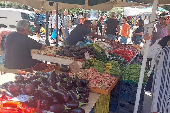 Vibrant Chania farmers market with fresh produce including eggplants, tomatoes, and beans under sunlit stalls.