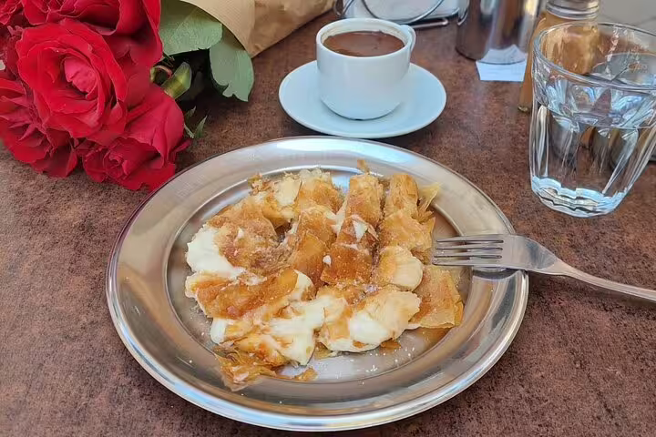 Indulge in Chania's Old Town with a traditional pastry and coffee, set beside vibrant red roses at a local café.