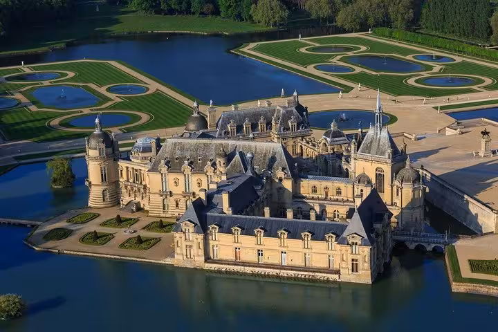 Aerial view of Château de Chantilly surrounded by moat and formal French gardens in Oise, France