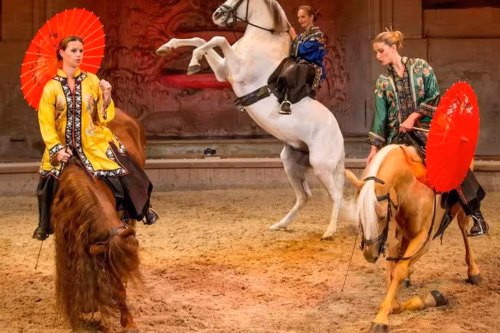 Elegant equestrian show with riders in ornate costumes holding red parasols on horses at Chantilly