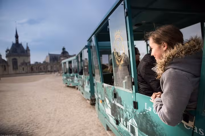 Woman leaning out of a green tourist train at Château de Chantilly on a sunny day