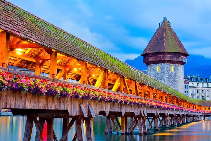 Chapel Bridge in Lucerne adorned with vibrant flowers, illuminated at dusk, ideal for Mount Titlis day trip tours.