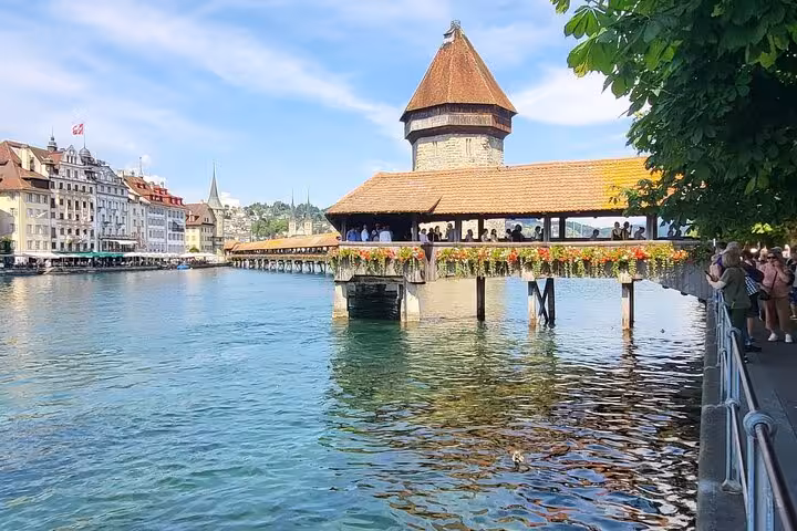 Iconic Chapel Bridge adorned with flowers over Reuss River in Lucerne, showcasing Swiss medieval architecture.