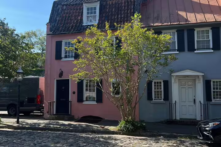 Historic pink and gray colonial row houses with black shutters on cobblestone street in Charleston, SC