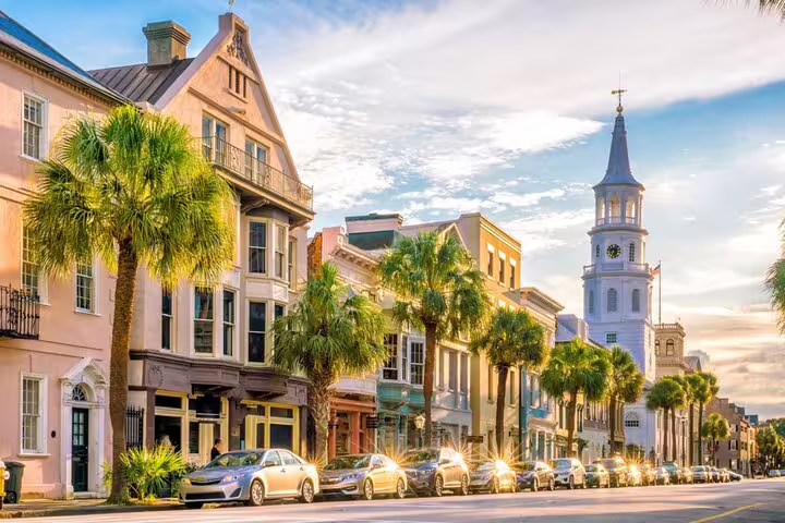 Historic Charleston street with palm trees, colorful colonial buildings, and St. Michael's Church steeple at golden hour