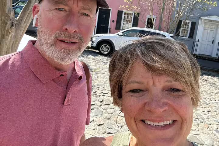 Couple taking selfie on historic cobblestone street in Charleston SC with colorful colonial buildings