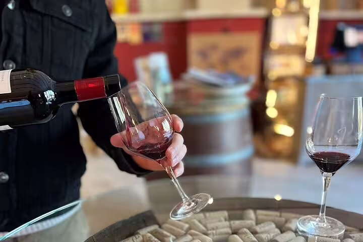 Sommelier pouring red wine into glass during Chateauneuf du Pape wine tasting with corks on barrel