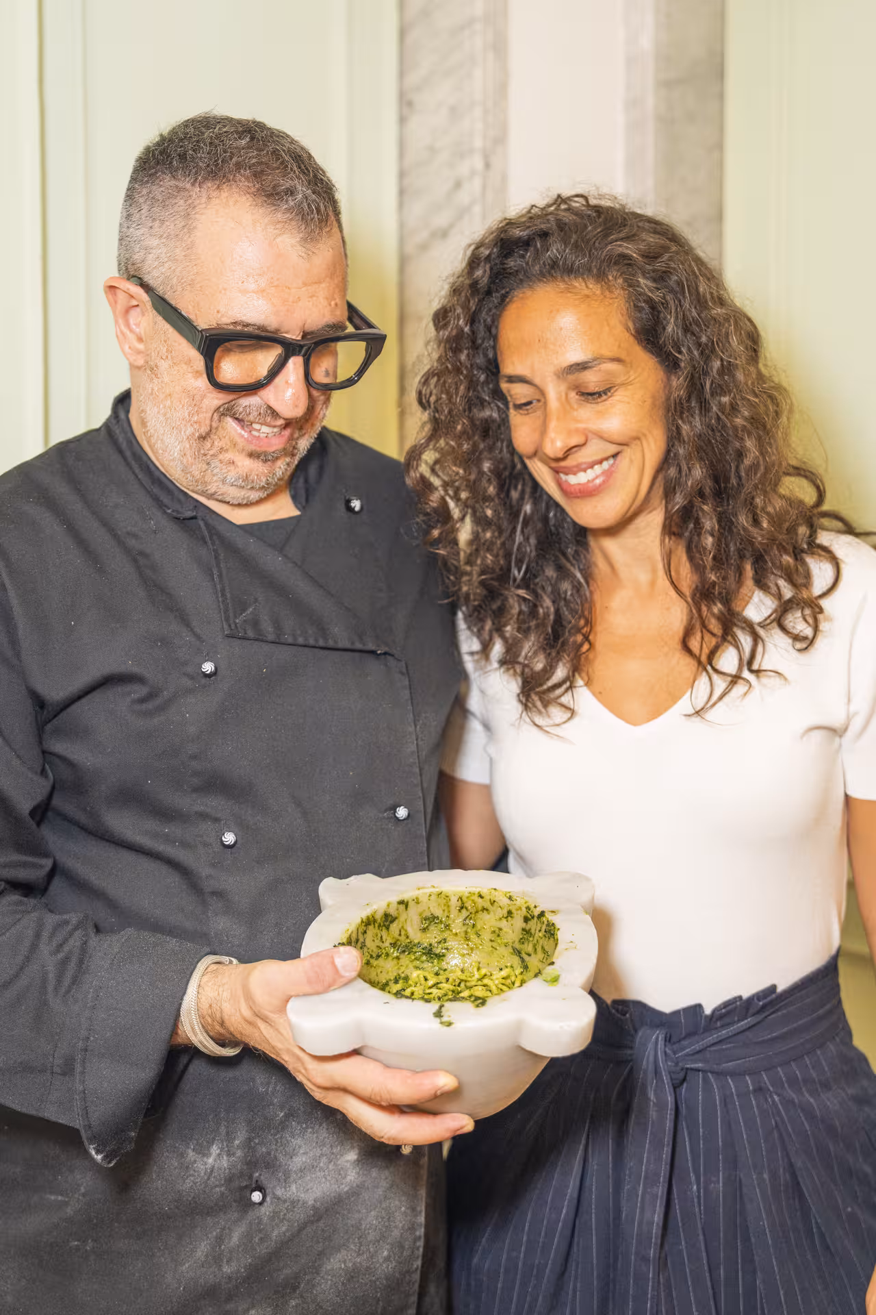 Chef and guest smiling while holding a mortar with freshly made pesto, showcasing culinary expertise at private dinners.