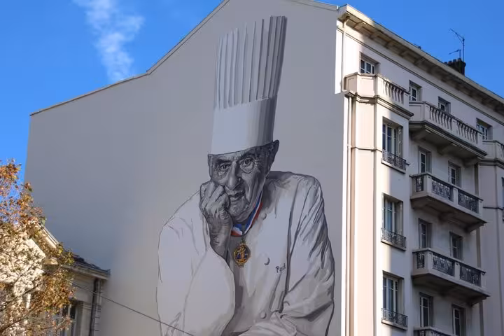 Mural of a chef on a building at Les Halles Paul Bocuse, adding cultural flair to the morning food market tour experience.