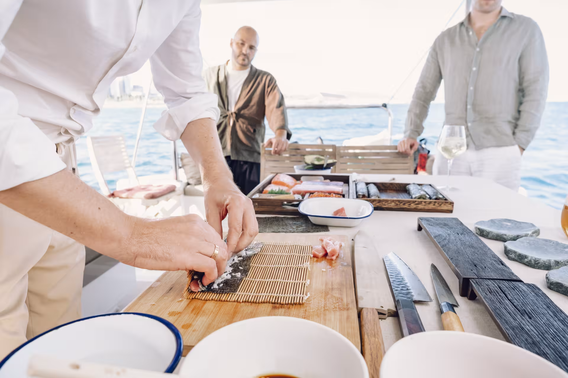 Chef rolling sushi on a bamboo mat aboard a yacht, hands-on sushi masterclass with sea view and fresh ingredients