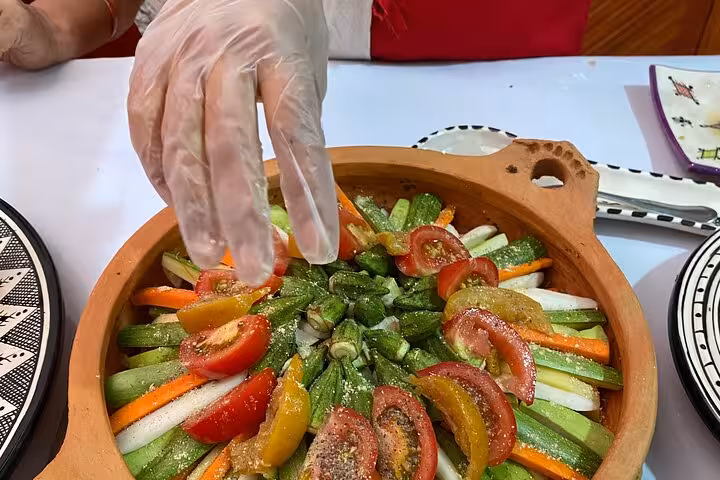 Chef in gloves seasoning a colorful vegetable dish in a rustic clay pot during a family cooking class experience.