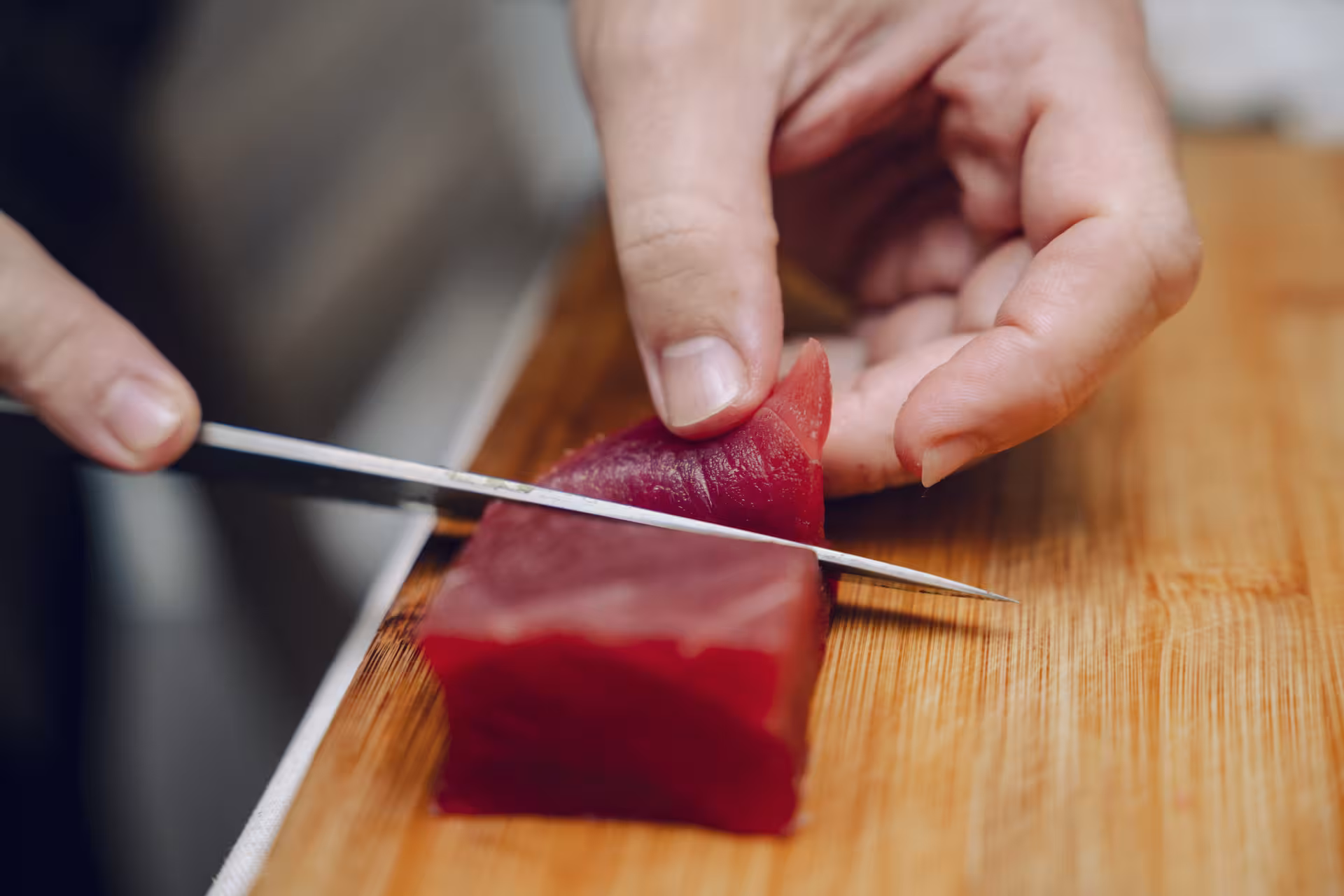 Close-up of chef slicing fresh tuna with a sushi knife on a cutting board during hands-on sushi masterclass