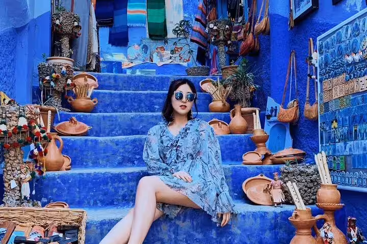 Traveler on Chefchaouen blue staircase with Moroccan pottery, highlight of 2-day trip from Casablanca