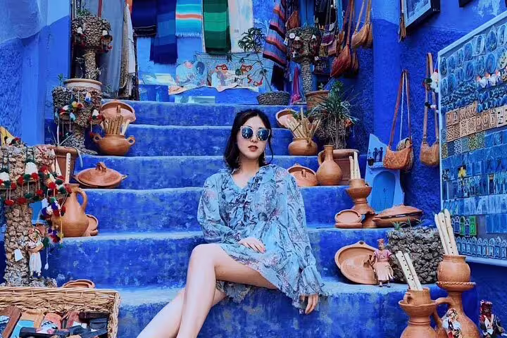 Traveler on Chefchaouen blue stairs with Moroccan pottery and souks, Morocco 12-day tour from Marrakech
