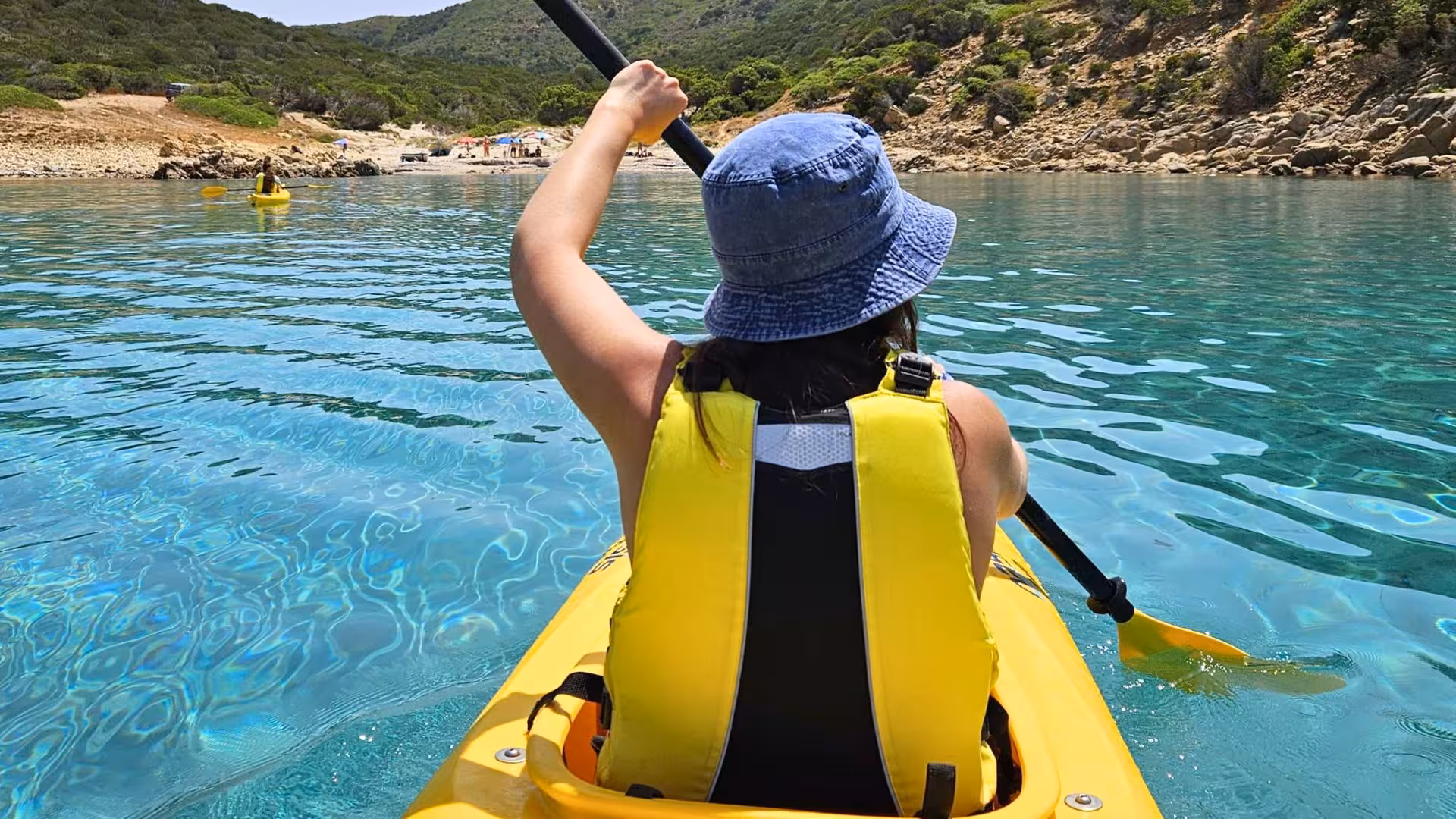 Solo kayaker paddling through vibrant blue waters towards Tuerredda beach on a sunny day.