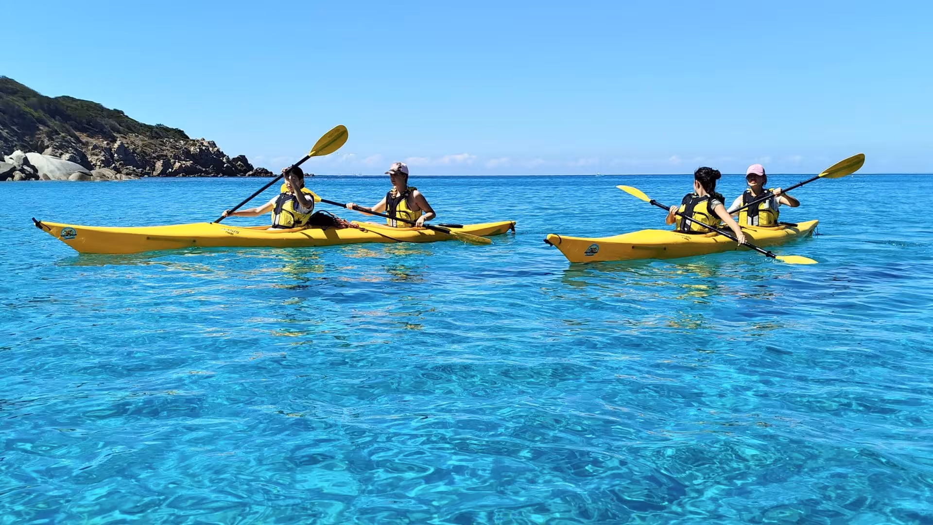 Kayakers enjoy a sunny tour in Tuerredda's crystal-clear waters, showcasing Chia's stunning coastal scenery.