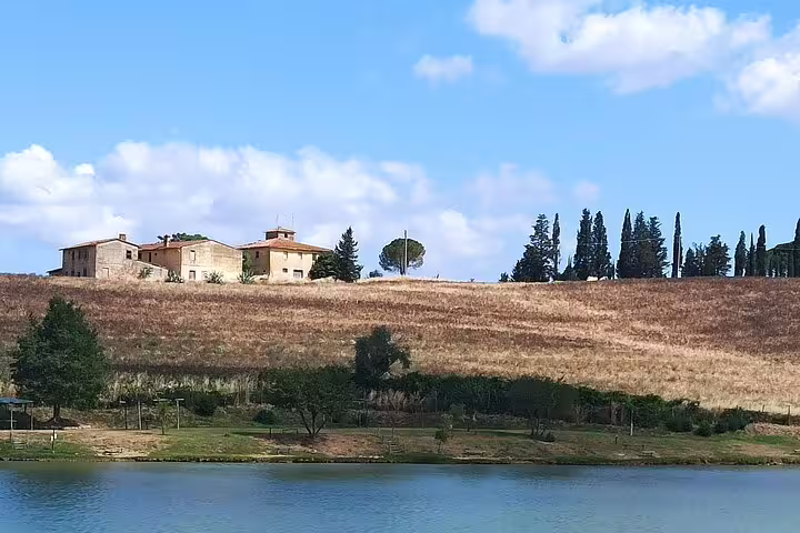 Stone farmhouse and cypress trees above a tranquil lake in the rolling Chianti Classico hills on a Tuscany morning wine tour