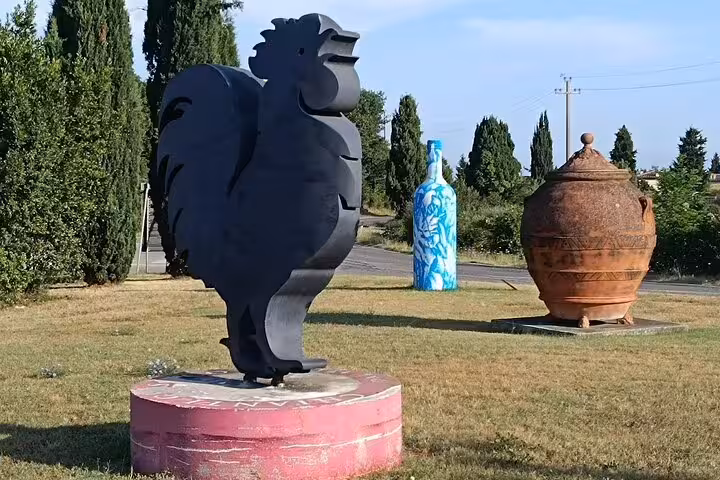 Iconic black rooster statue with giant wine bottle and terracotta jar marking Chianti Classico wine region on Good Morning tour route