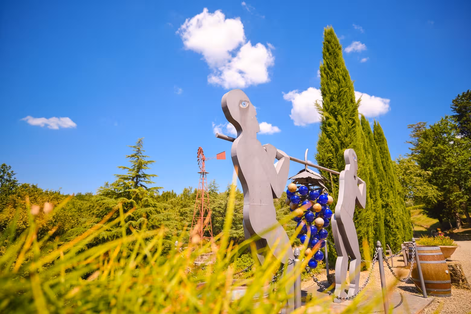 Sculptures amid lush greenery in Chianti vineyard under a bright blue sky, showcasing Tuscan art and nature.