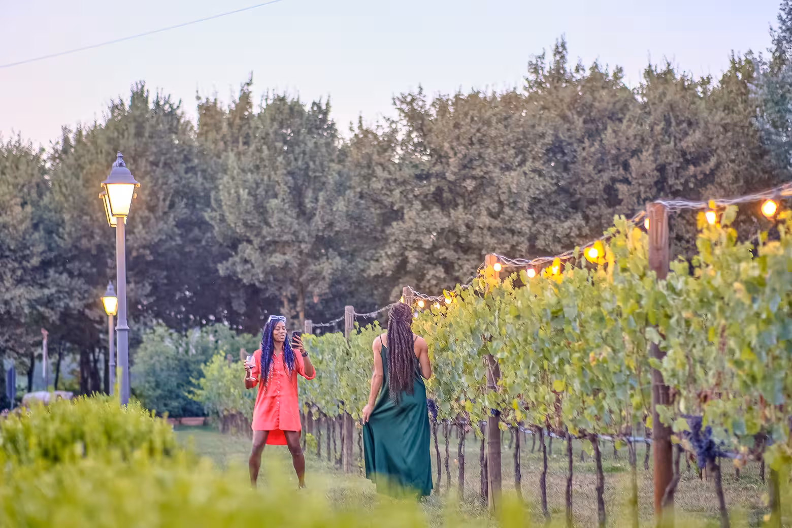 Two women enjoying a scenic walk through a vineyard in Chianti during the Siena Wine Tour at sunset.