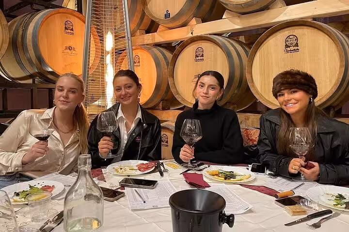 Group enjoying wine tasting at a Chianti winery with oak barrels in the background.